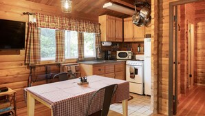Une cuisine chaleureuse, aménagée dans le style d’un chalet, avec des murs en bois, une table à manger recouverte d’une nappe à carreaux et les appareils de cuisine de base.