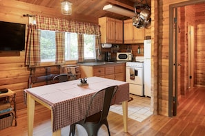 Une cuisine chaleureuse, aménagée dans le style d’un chalet, avec des murs en bois, une table à manger recouverte d’une nappe à carreaux et les appareils de cuisine de base.