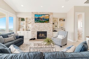 A living room with a stone fireplace, a sofa, a patterned armchair, and a bookshelf.