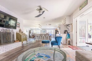 Uma sala de estar ampla com uma mesa de centro de vidro, uma poltrona azul e uma cozinha moderna ao fundo.