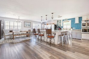 Cozinha ampla com ilha central, banquetas e área de refeições com banco e cadeiras.