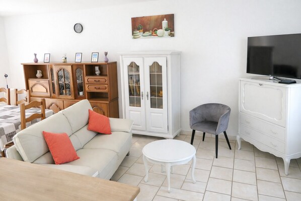 A living room with a sofa, a chair, a white cabinet, a television, and a painting on the wall.