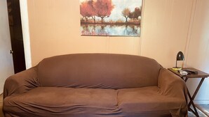 En brun soffa i ett rum med en tavla som föreställer träd på väggen.
