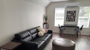 A modern living room with a black leather sofa, a round ottoman, a small side table, and a dining area with two chairs. - Spacious 1bd/1bt downtown apartment next to the park (Vancouver)
