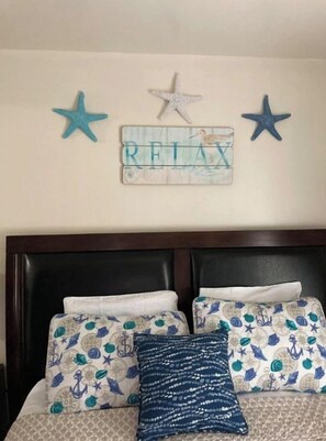 Quarto com cama, almofadas estampadas e um adorno de parede com estrelas e a palavra 'RELAX'.