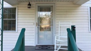 Ett vitt hus med en ytterdörr, en vit gungstol och en välkomstmatta.