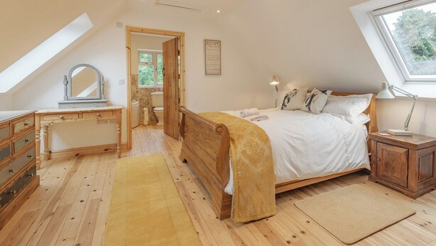 A bedroom with a wooden bed, a desk with a mirror, a window, and a skylight.