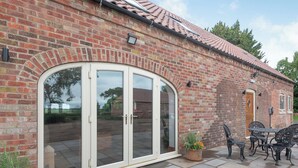 A brick building with a large glass door, outdoor seating, and a tiled roof.