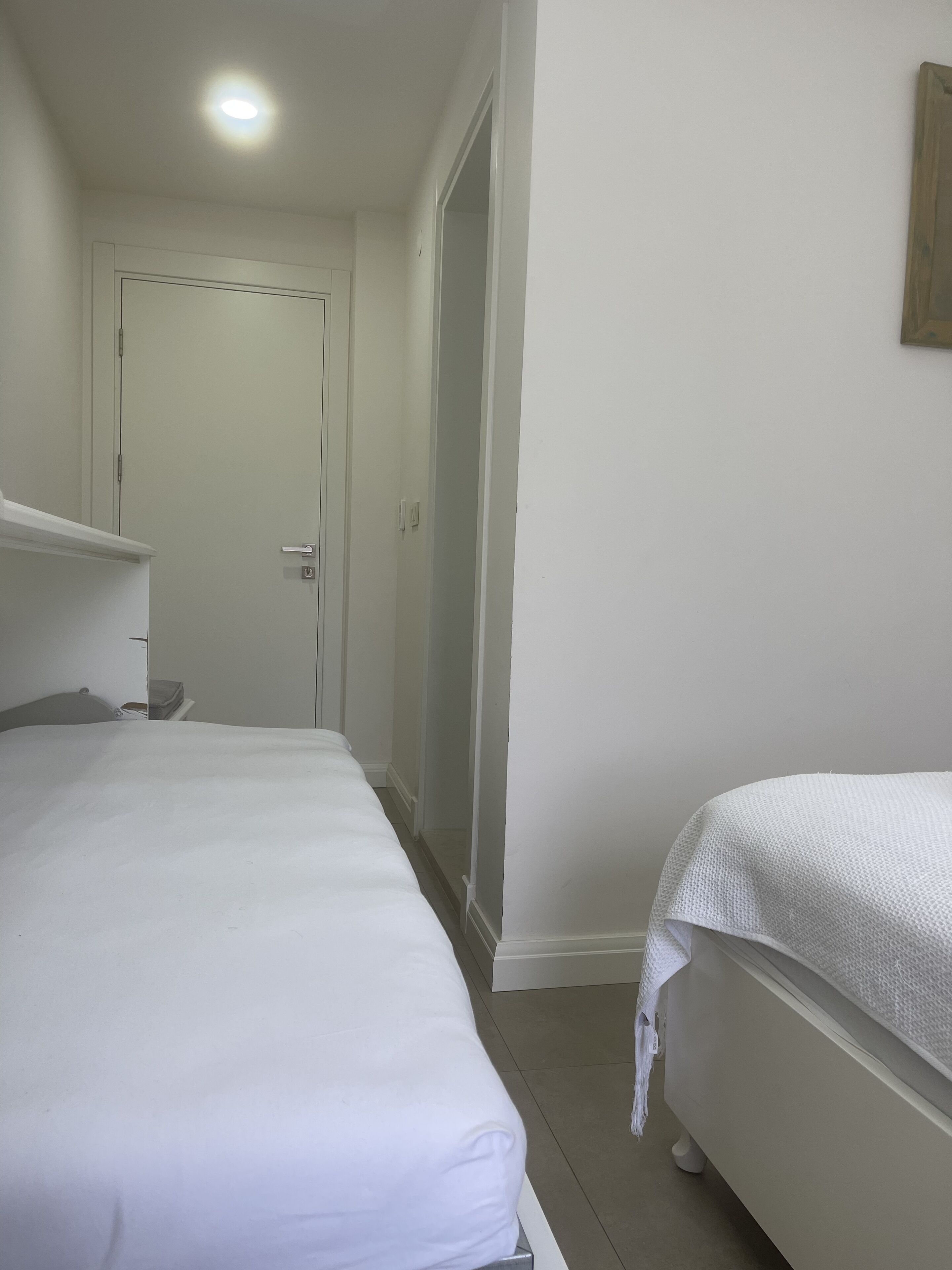 A narrow hotel room with two single beds, a door, and a small shelf.
