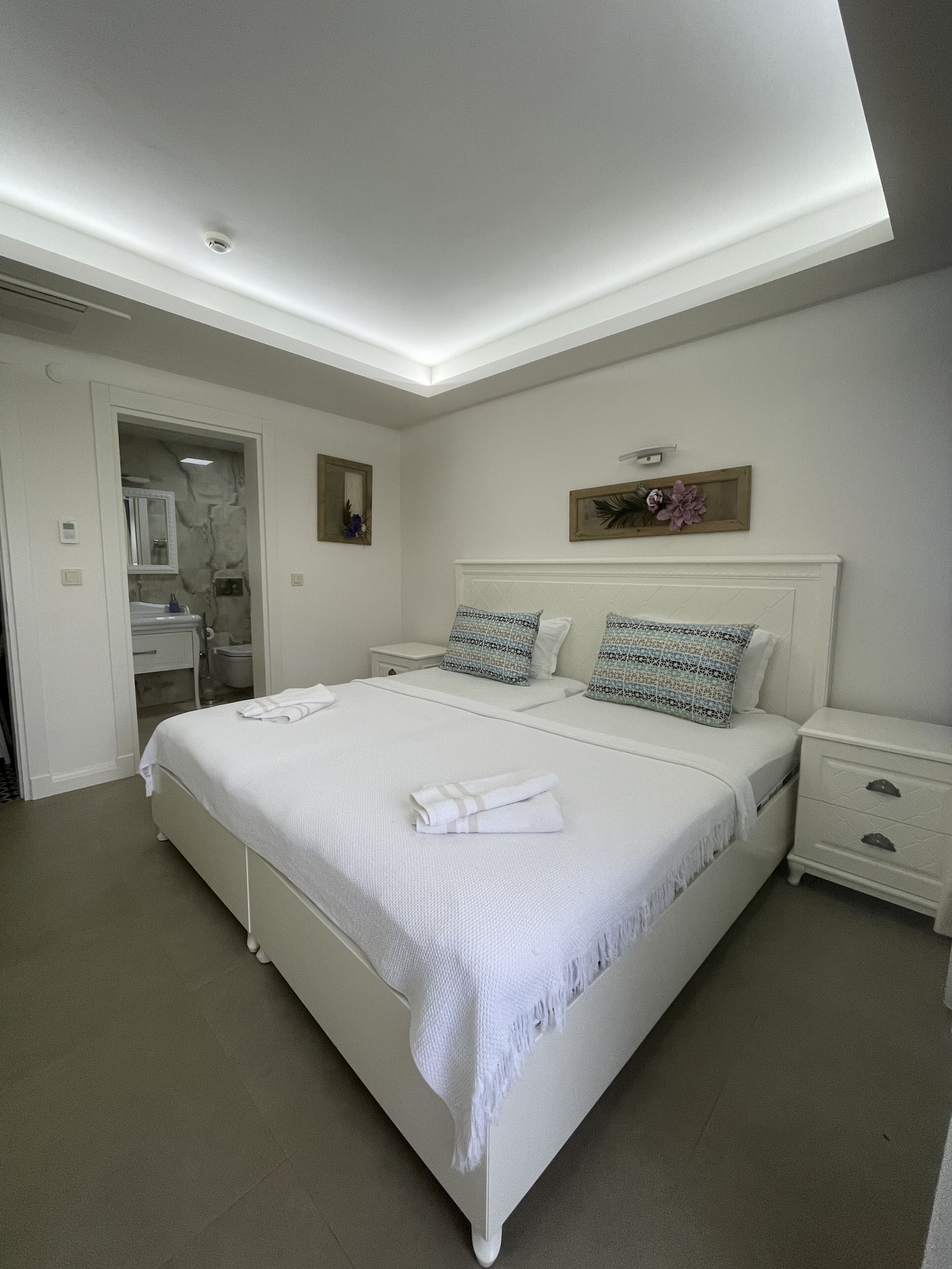 A neatly arranged bedroom with a large bed, bedside tables, a nightstand, and a bathroom visible through an open door.