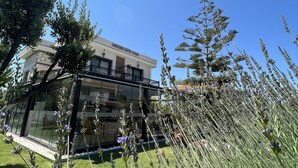 A modern building with a glass facade and a balcony, surrounded by a well-maintained lawn and lavender plants. - Dalyan Risus Suite (Cesme)