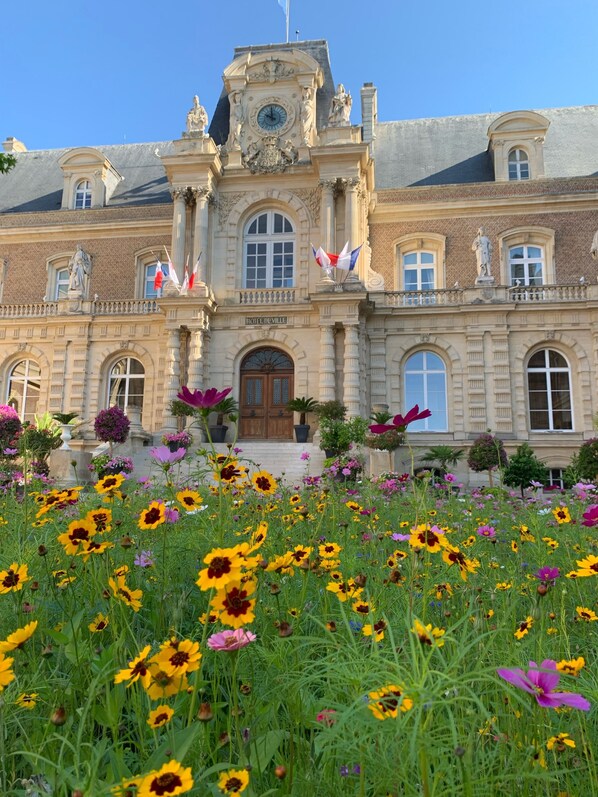 A historic building with a clock tower, a central entrance, and a garden with sunflowers.
