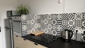 Een keuken met een zwart aanrecht, een magnetron, een waterkoker en een betegelde achterwand.