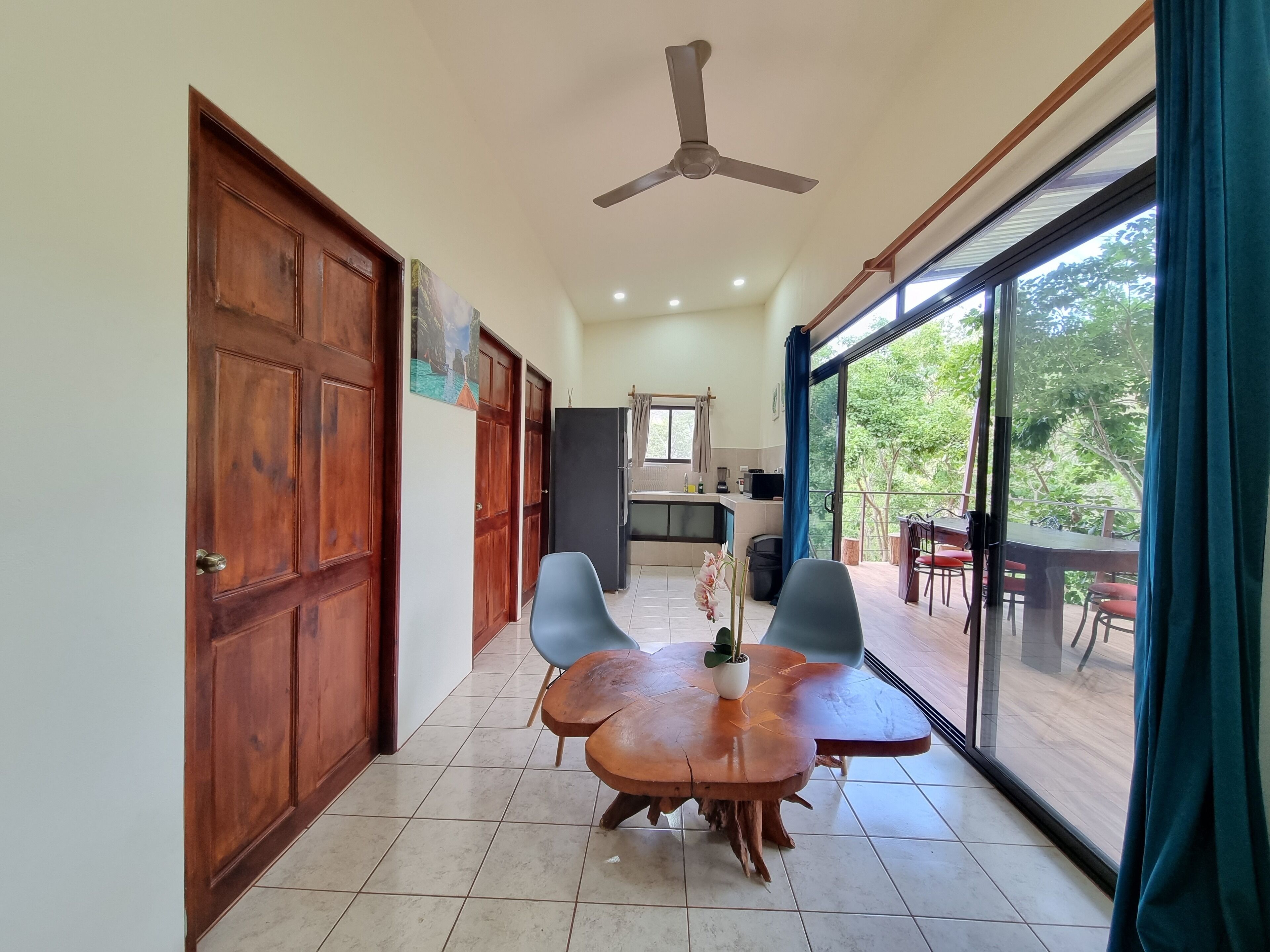 Una habitación amplia con una mesa de comedor de madera y sillas, un ventilador de techo y vistas a un balcón con mobiliario de exterior.