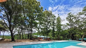 A swimming pool surrounded by trees and a building with outdoor seating. - Romantic Villa Anturio at Pinilla Highlands with Amazing Canopy views (Guanacaste Province)