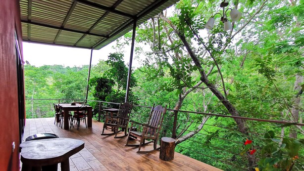 A wooden deck with a table and chairs, surrounded by lush greenery and trees. - Romantic Villa Anturio at Pinilla Highlands with Amazing Canopy views (Guanacaste Province)