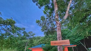 A red building with a blue roof, surrounded by lush greenery and trees. A wooden sign with "Villa Antwio" is visible. - Romantic Villa Anturio at Pinilla Highlands with Amazing Canopy views (Guanacaste Province)