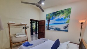 A bedroom with a bed, a wooden wardrobe, a ceiling fan, a painting of a beach, and a floor lamp. - Romantic Villa Anturio at Pinilla Highlands with Amazing Canopy views (Guanacaste Province)