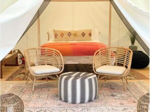 Cozy bedroom with a pitched roof, featuring a bed, two wicker chairs, and a potted plant.