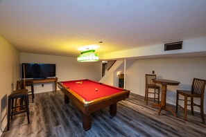 A pool table with a red felt surface, wooden chairs, and a television on a stand. - The Holston River House - a Sojourn in Serenity (Marion)