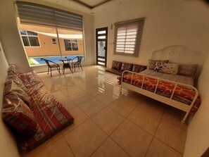Een kamer met een bed, een bank, een kleine tafel en stoelen. Er is een raam met zonwering en uitzicht op het omliggende landschap.