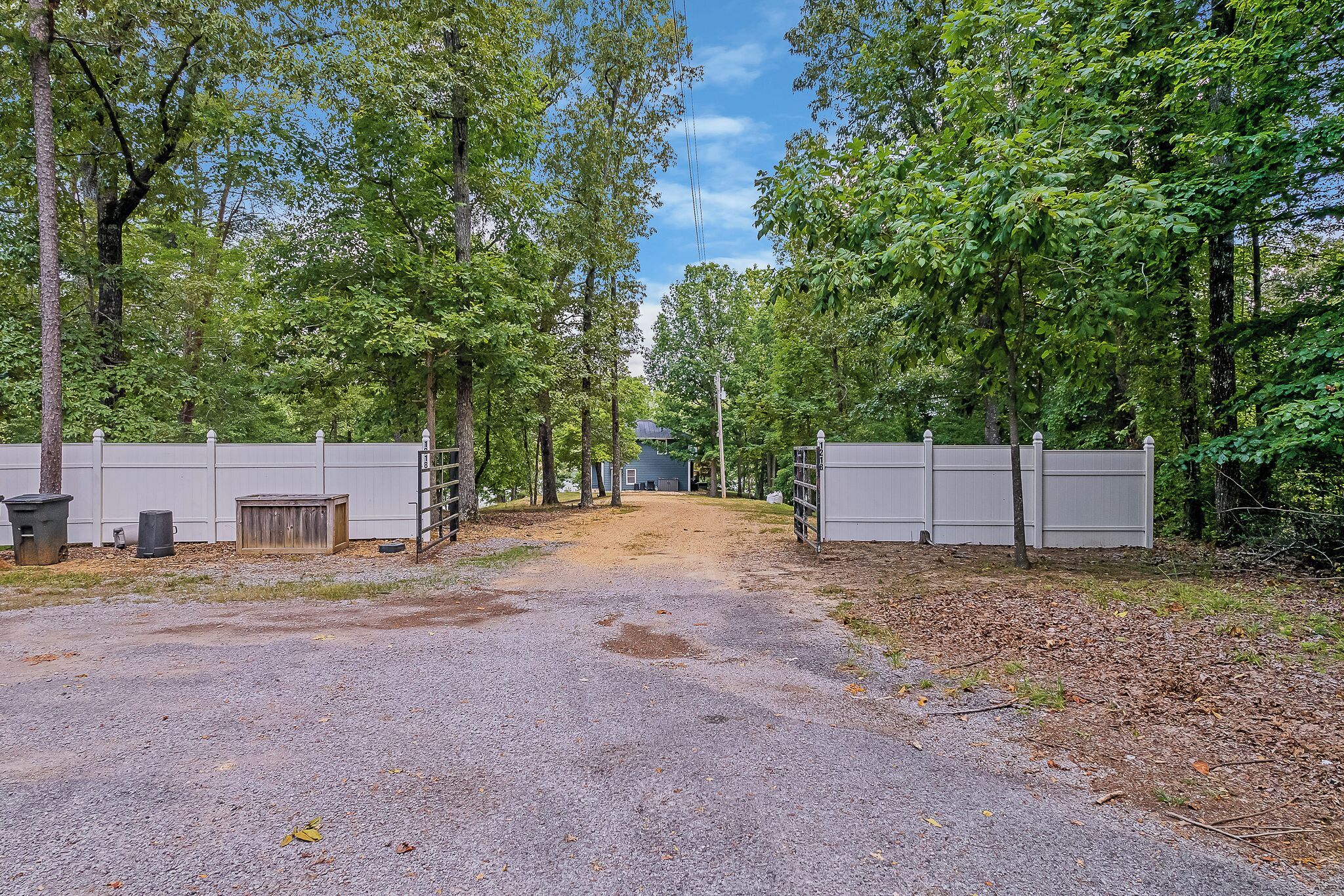 A gravel driveway leading to a gated area with a house in the background.