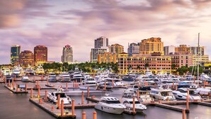 A marina with numerous yachts docked, a city skyline in the background, and a clear sky. - Modern Romantic Tropical Poolside Retreat! (West Palm Beach)