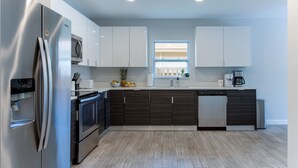 A modern kitchen with stainless steel appliances, dark wood cabinets, and a light wood floor. - Modern Romantic Tropical Poolside Retreat! (West Palm Beach)