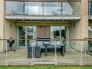 Et moderne hus med to etager, en balkon, udendørs møbler og en grill.