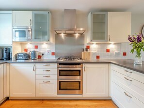 Una cocina moderna con electrodomésticos de acero inoxidable, armarios blancos y una campana extractora central.