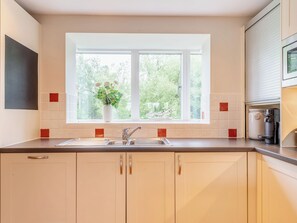A kitchen with a window, a sink, cabinets, and a coffee maker.