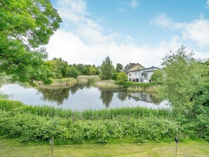 A house by a pond with surrounding greenery.
