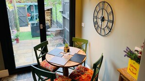 A dining area with a table and chairs, a clock on the wall, and a view of the backyard through a glass door.