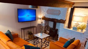 A cozy living room with orange sofas, a flat-screen TV, a stone wall, a fireplace, and a 'Be our guest' sign.