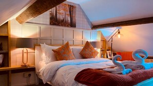 A bedroom with a bed, pillows, a lamp, a blanket, and a painting on the wall.