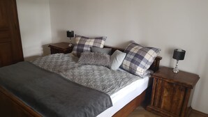 Una cama bien hecha con una colcha gris y varios almohadones, flanqueada por dos mesitas de noche con lámparas.
