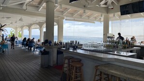 Ein großzügiger Außenbereich mit Bar und Meerblick, mit hohen Decken, Holzbalken und verschiedenen Sitzgelegenheiten.