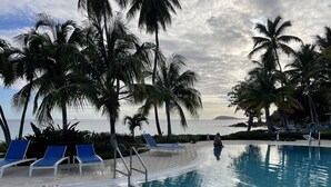 Ein Poolbereich mit Liegestühlen und Palmen, mit Blick auf ein Gewässer.