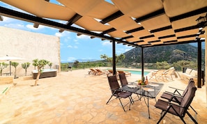 An outdoor patio with a pool, lounge chairs, and a table with fruit and drinks.
