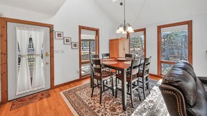 A dining area with a wooden table and chairs, a chandelier, and large windows offering a view of the outdoors. - Jim Thorpe, Bear Creek Lake, Cozy 3Br family friendly home- EV charging outlet (Jim Thorpe)