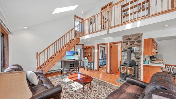 A spacious living area with a high ceiling, a wooden staircase, a stone fireplace, and a television. - Jim Thorpe, Bear Creek Lake, Cozy 3Br family friendly home- EV charging outlet (Jim Thorpe)