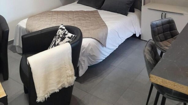 Een moderne slaapkamer met een bed, een bureau en een stoel. Er hangen wandlampen en een lijst met een afbeelding boven het bed.