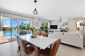 Un grand espace de vie comprenant une table à manger, un canapé et donnant sur une piscine et un jardin.