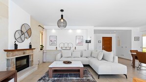 A modern living room with a fireplace, a white sectional sofa, a coffee table, and a dining area with a wooden table and chairs.