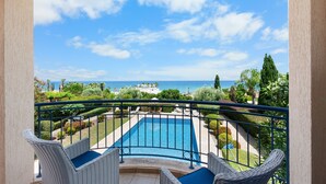 A balcony with wicker chairs and a pool, overlooking a beach and ocean.