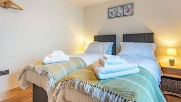 A double bed with two pillows, a bedside table with a lamp, and a wall-mounted light fixture.