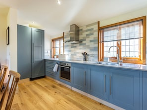 A modern kitchen with blue cabinets, a stainless steel sink, and wooden flooring. - Snowdrop Lodge -UK32959 (Ashford)