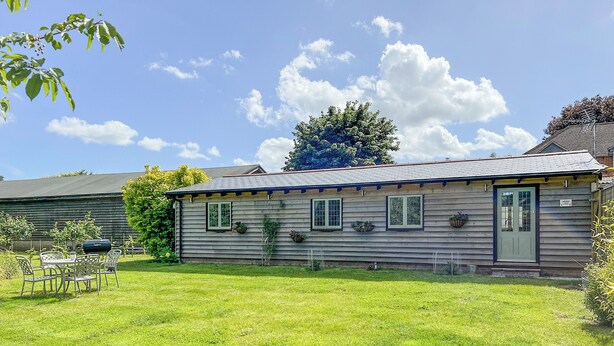 A wooden house with a front porch, a dining table and chairs, and a well-maintained lawn.