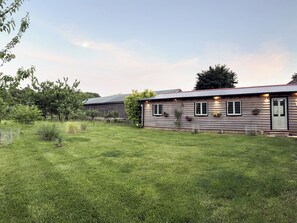 A rustic wooden house with a well-maintained lawn, surrounded by trees and a fence. - Snowdrop Lodge -UK32959 (Ashford)