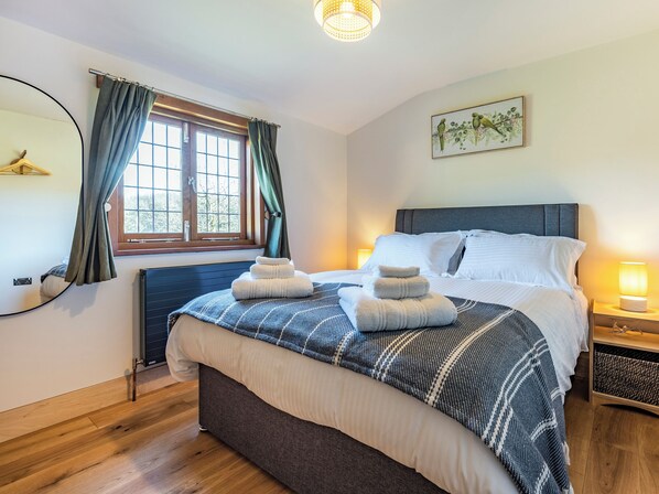 A neatly made bed with a blue and white checkered blanket, a bedside lamp, and a window with curtains. - Snowdrop Lodge -UK32959 (Ashford)
